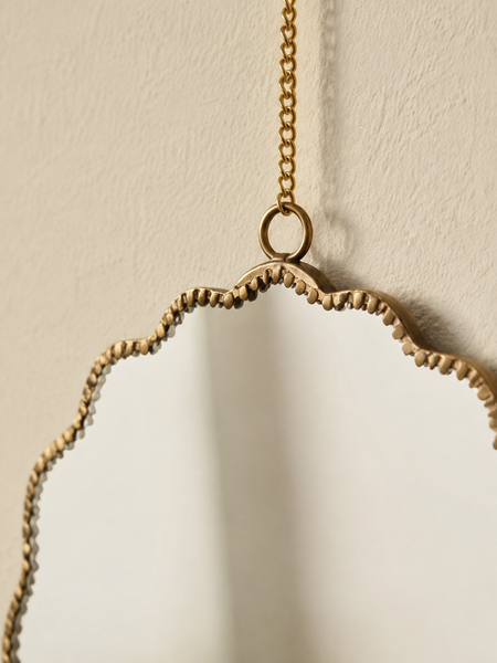 Detalle del marco dorado y cadena de un espejo decorativo con forma de concha