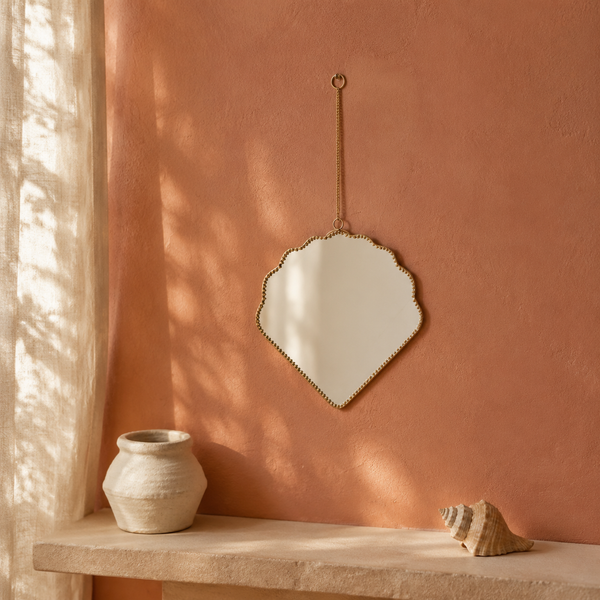 Espejo con forma de concha y cadena dorada sobre pared color terracota