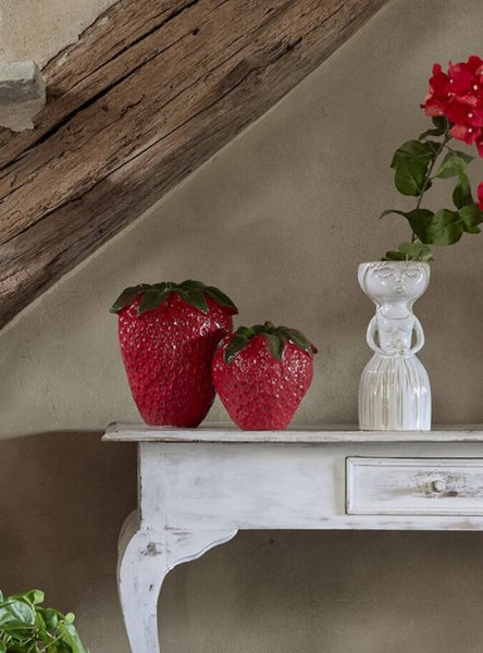 Jarrón decorativo de cerámica con forma de fresa colocado sobre una consola de madera.