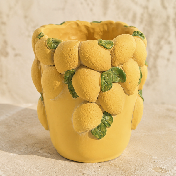 Jarrón de cemento amarillo con limones y hojas verdes en relieve sobre fondo de piedra clara