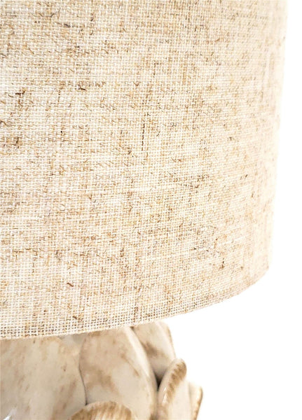 Detalle de la pantalla de tejido beige con textura natural y la base de cerámica con hojas superpuestas de la lámpara Piña.