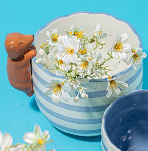 Macetero de porcelana con perro salchicha decorado con flores blancas.